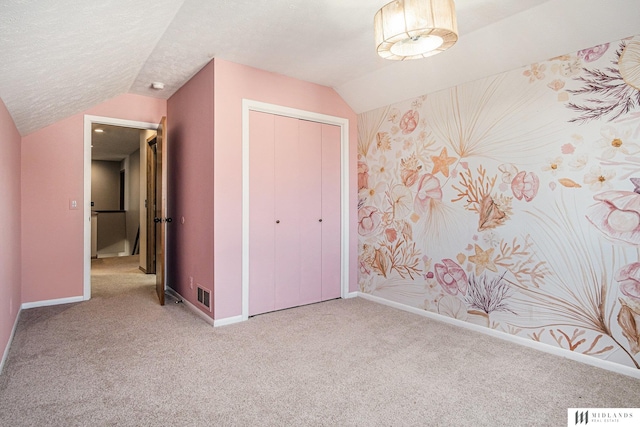 unfurnished bedroom with light carpet, baseboards, vaulted ceiling, a textured ceiling, and a closet