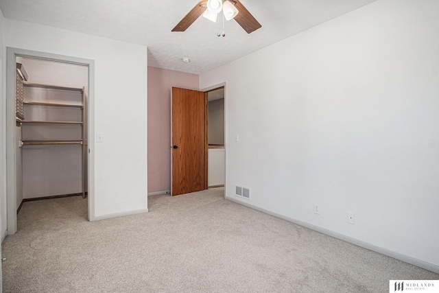 unfurnished bedroom featuring light carpet, a walk in closet, visible vents, and baseboards