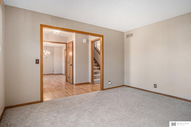 unfurnished room featuring a notable chandelier, light colored carpet, visible vents, baseboards, and stairs