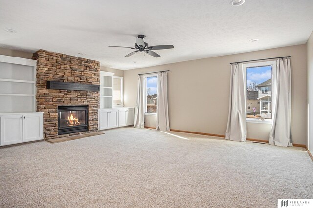 unfurnished living room with built in features, baseboards, light colored carpet, a textured ceiling, and a stone fireplace