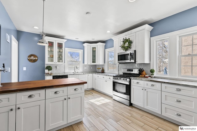 kitchen featuring decorative light fixtures, appliances with stainless steel finishes, glass insert cabinets, white cabinetry, and wood counters