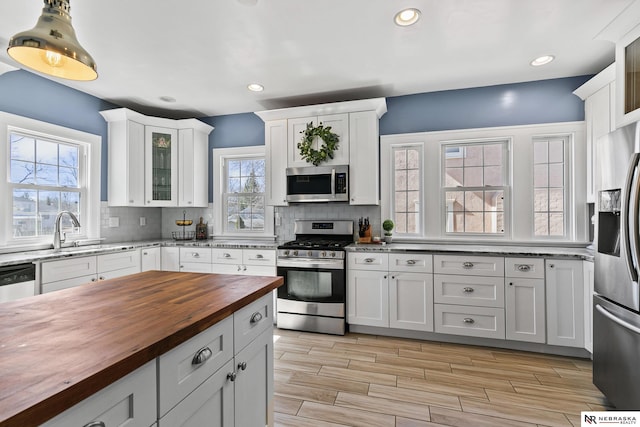 kitchen featuring tasteful backsplash, appliances with stainless steel finishes, glass insert cabinets, white cabinetry, and butcher block countertops