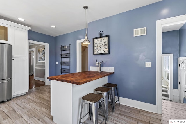 kitchen with stainless steel fridge, visible vents, butcher block counters, hanging light fixtures, and white cabinetry