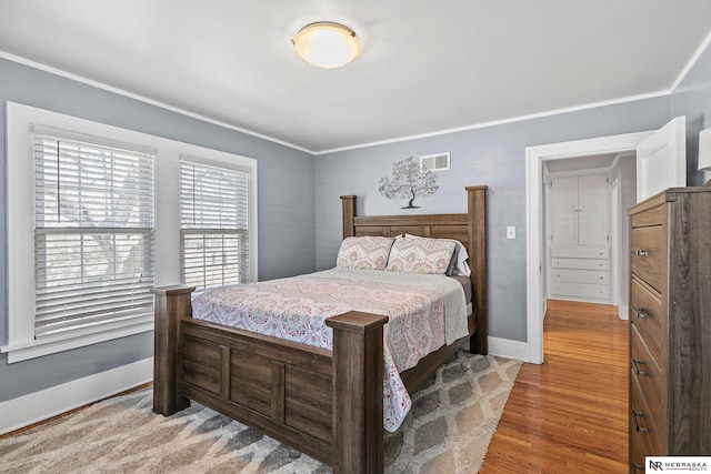 bedroom with baseboards, ornamental molding, visible vents, and light wood-style floors