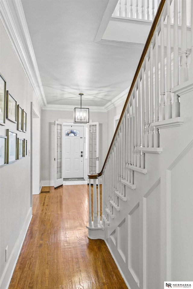 entryway featuring wood-type flooring, stairway, an inviting chandelier, ornamental molding, and baseboards