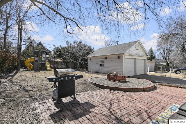 view of patio with an outbuilding, a playground, a detached garage, fence, and area for grilling