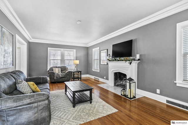 living room with crown molding, visible vents, a fireplace with flush hearth, wood finished floors, and baseboards