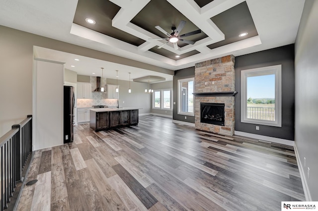 living room with baseboards, coffered ceiling, ceiling fan, wood finished floors, and a stone fireplace