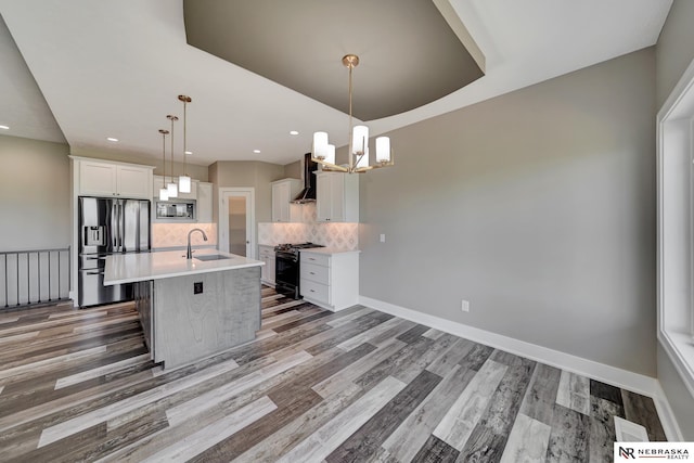 kitchen with range with gas stovetop, stainless steel refrigerator with ice dispenser, a kitchen island with sink, built in microwave, and wall chimney exhaust hood