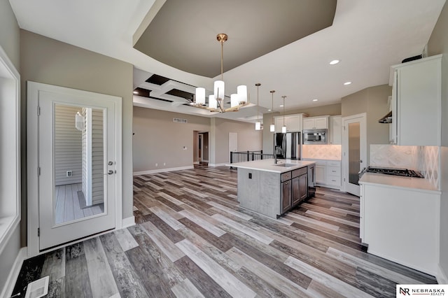 kitchen with a kitchen island with sink, open floor plan, light countertops, appliances with stainless steel finishes, and pendant lighting