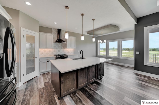 kitchen with light countertops, wall chimney range hood, black appliances, and white cabinets