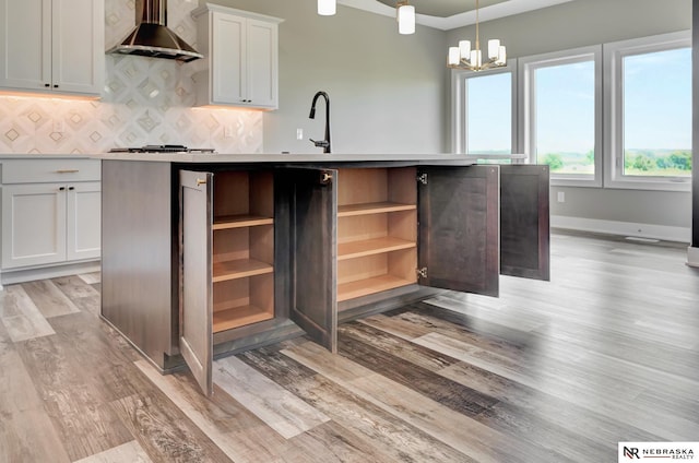 kitchen featuring a kitchen island with sink, white cabinetry, light countertops, wall chimney range hood, and pendant lighting