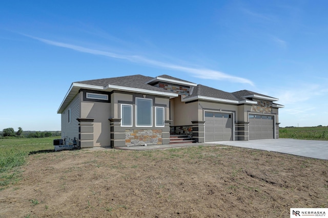 prairie-style home with a garage, concrete driveway, stone siding, stucco siding, and a front yard