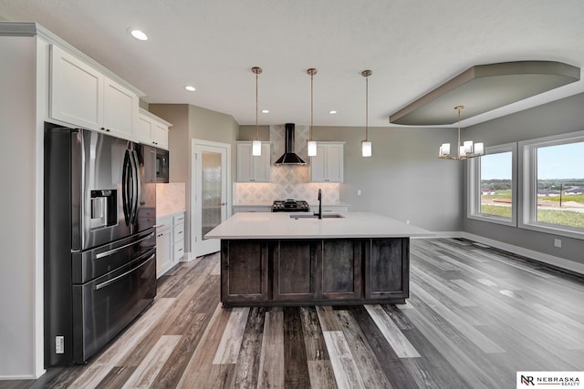 kitchen with white cabinets, stainless steel fridge with ice dispenser, wall chimney exhaust hood, light countertops, and pendant lighting