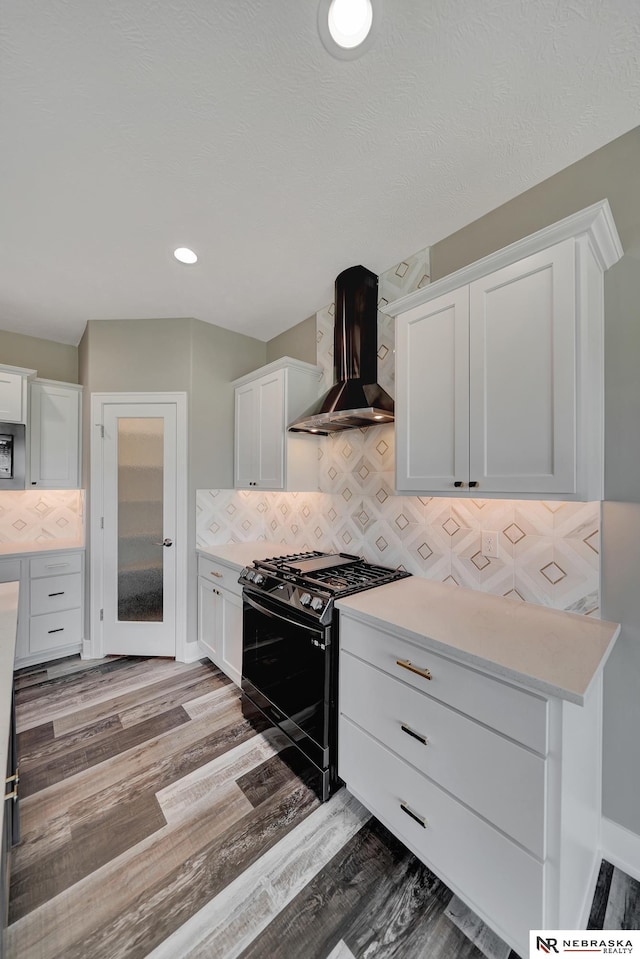 kitchen with white cabinetry, light countertops, wall chimney range hood, backsplash, and gas range oven