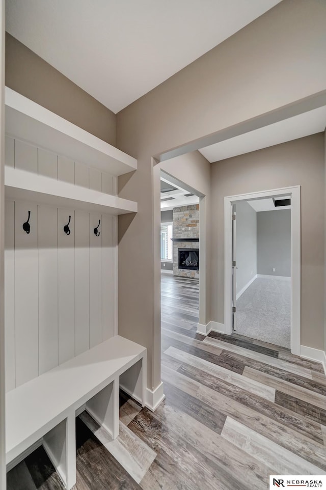 mudroom with a stone fireplace, baseboards, and wood finished floors