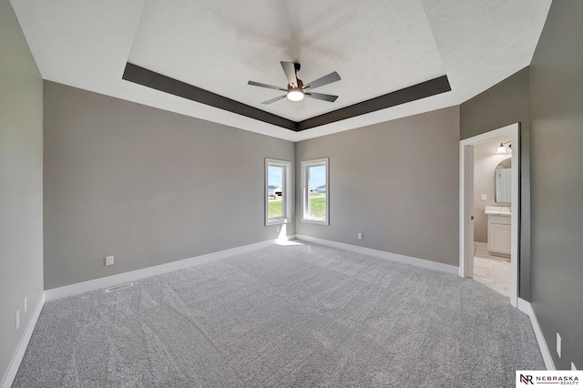 unfurnished bedroom featuring light carpet, baseboards, a tray ceiling, and a textured ceiling