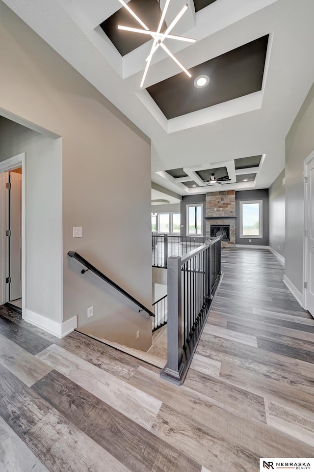 staircase featuring a chandelier, a fireplace, wood finished floors, baseboards, and a raised ceiling