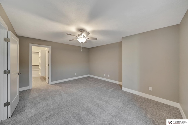 unfurnished bedroom with baseboards, a walk in closet, a ceiling fan, and light colored carpet