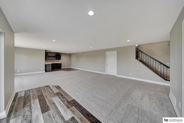 unfurnished living room featuring stairs, recessed lighting, light colored carpet, and baseboards