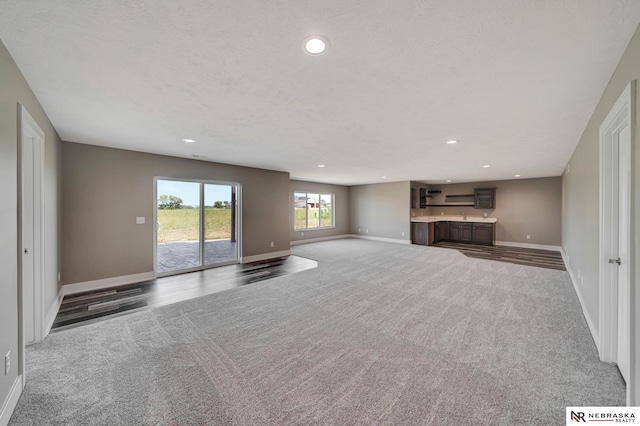 unfurnished living room with a textured ceiling, dark colored carpet, and baseboards