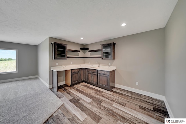 kitchen featuring open shelves, light countertops, a sink, dark brown cabinets, and baseboards