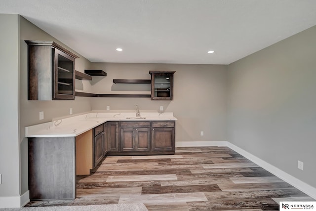 kitchen with dark brown cabinetry, a sink, light wood-type flooring, open shelves, and glass insert cabinets