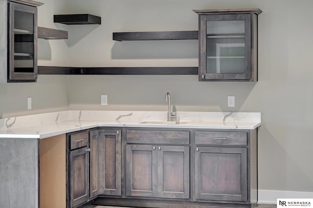 kitchen featuring glass insert cabinets, a sink, light stone counters, and open shelves