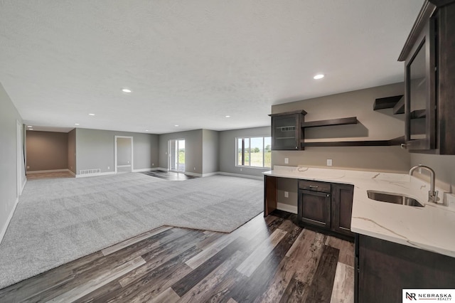 kitchen featuring a sink, open floor plan, dark brown cabinets, open shelves, and glass insert cabinets