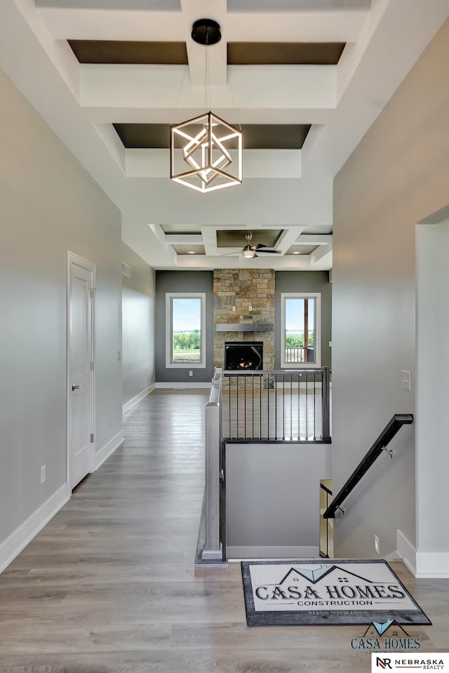 staircase featuring a healthy amount of sunlight, coffered ceiling, wood finished floors, and a stone fireplace