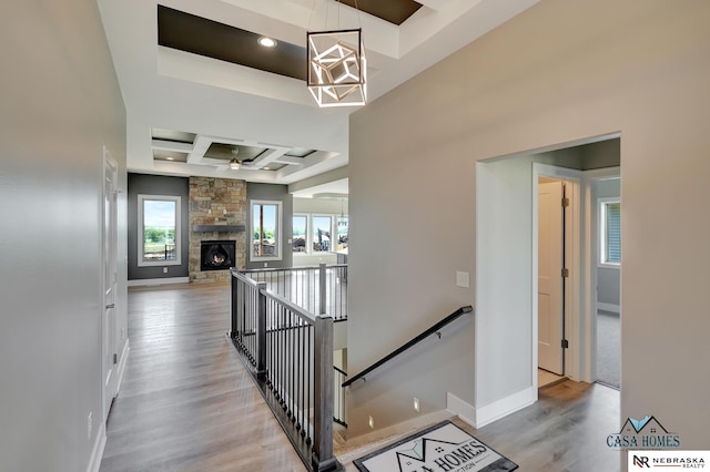 corridor with beam ceiling, light wood-style floors, an upstairs landing, coffered ceiling, and baseboards