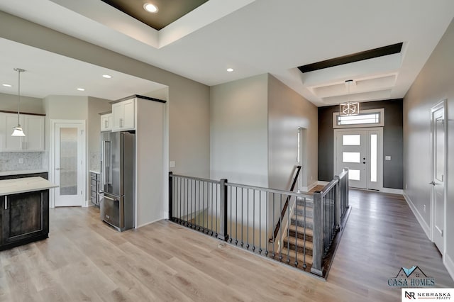 interior space with a tray ceiling, baseboards, light wood-style flooring, and an upstairs landing