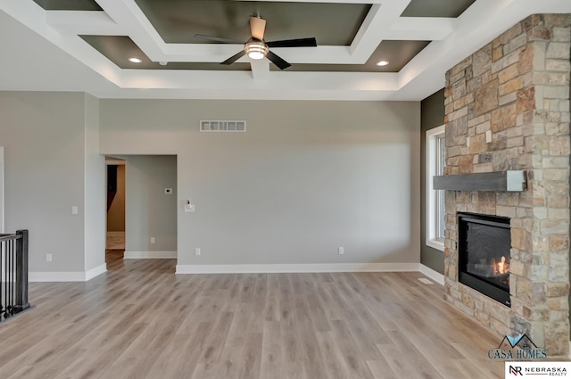 unfurnished living room with a stone fireplace, coffered ceiling, visible vents, baseboards, and light wood-type flooring