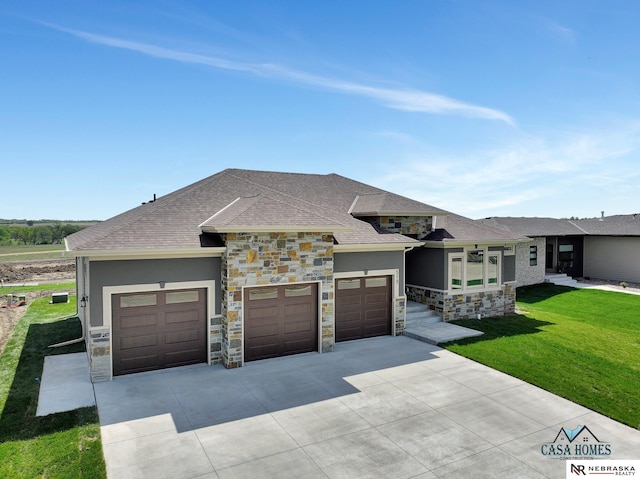 prairie-style house with roof with shingles, a garage, stone siding, driveway, and a front lawn