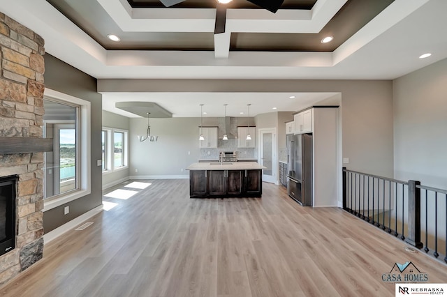 kitchen with a center island with sink, hanging light fixtures, light countertops, wall chimney range hood, and high end fridge