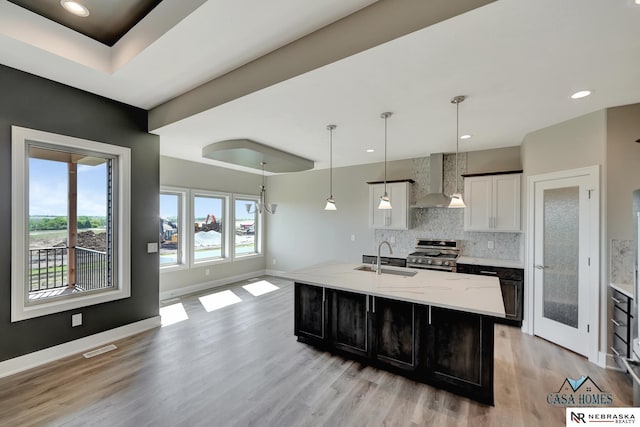 kitchen featuring a sink, white cabinets, high end stainless steel range, an island with sink, and pendant lighting