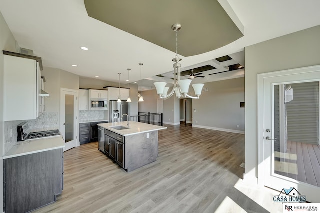 kitchen featuring light countertops, hanging light fixtures, white cabinets, a kitchen island with sink, and built in microwave