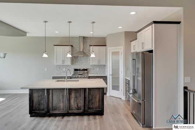 kitchen with premium appliances, an island with sink, wall chimney range hood, and decorative light fixtures