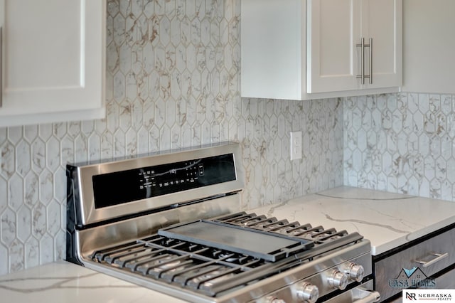 kitchen with light stone countertops, tasteful backsplash, stainless steel range with gas cooktop, and white cabinetry