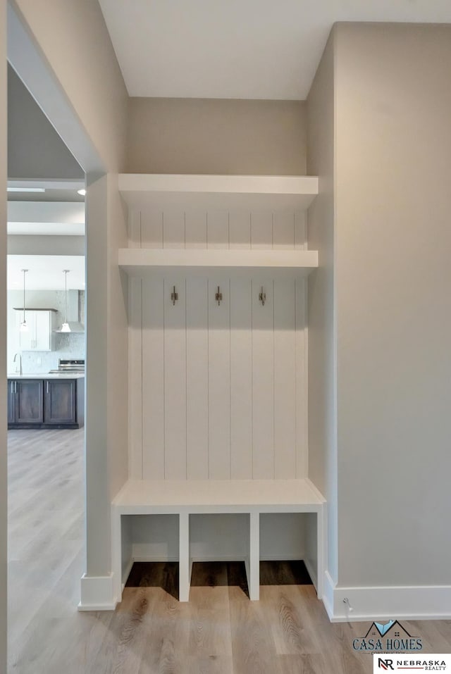 mudroom featuring light wood-type flooring, a sink, and baseboards