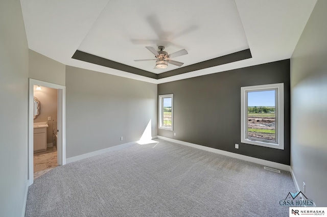 carpeted spare room featuring a tray ceiling, visible vents, and baseboards