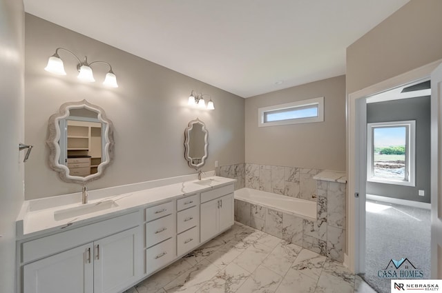 full bathroom with marble finish floor, double vanity, a sink, and a bath