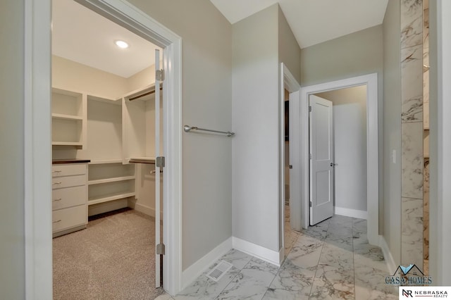 bathroom with marble finish floor, a walk in closet, and baseboards