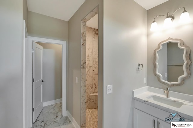 bathroom featuring marble finish floor, baseboards, a tile shower, and vanity