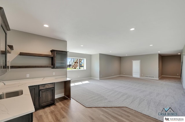 kitchen with light stone counters, open shelves, visible vents, open floor plan, and a sink