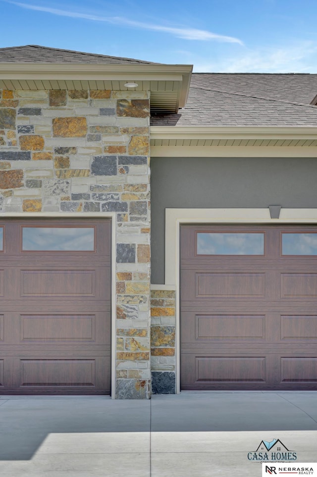 exterior space with a garage, stone siding, a shingled roof, and concrete driveway