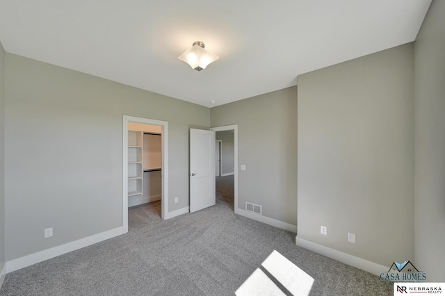 unfurnished bedroom with carpet floors, visible vents, baseboards, a closet, and a walk in closet