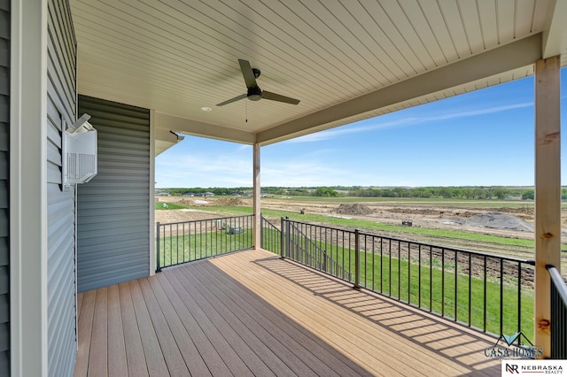 wooden deck with a ceiling fan, a rural view, and a yard