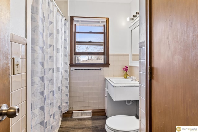 bathroom featuring a wainscoted wall, tile walls, visible vents, toilet, and a shower with curtain