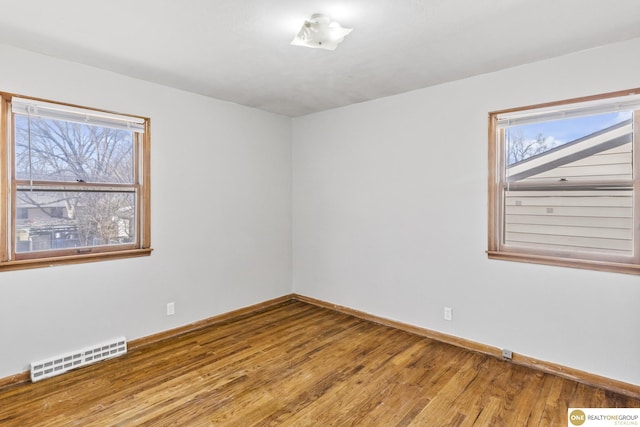 spare room with wood-type flooring, visible vents, and baseboards